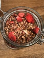 Domowa granola z kawałkami liofilizowanej truskawki Johny Catch w szklanym słoiku na drewnianym blacie.