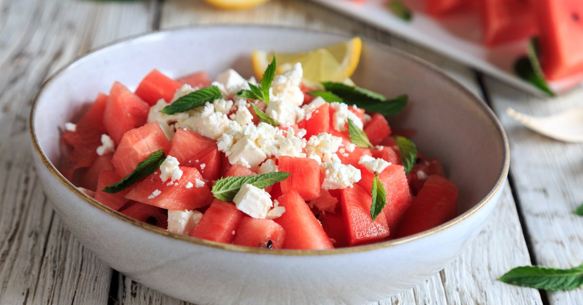 Miseczka z pokrojonym liofilizowanym arbuzem, kawałkami sera feta i świeżymi listkami bazylii. Kompozycja prezentuje się lekko i kolorowo – idealna letnia przekąska.