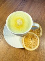 Filiżanka napoju Matcha + Orange Zen Johny Catch z pianką w odcieniu zieleni i plasterkami liofilizowanej pomarańczy na spodku – naturalna matcha z cytrusową nutą.