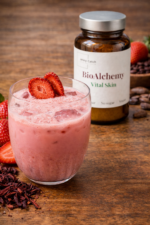 BioAlchemy Vital Skin – różowy napój superfood z truskawką w szklance, opakowanie produktu w tle