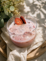 Różowe smoothie truskawkowe z liofilizowanymi truskawkami BIO Johny Catch, podane z lodem w szklance na naturalnej tkaninie.